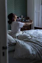 Young woman stretching arms sitting on bed at home - WPEF06838