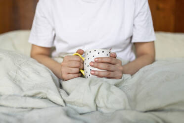 Hände einer jungen Frau, die eine Kaffeetasse hält und zu Hause auf dem Bett sitzt - WPEF06839