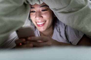 Glückliche Frau mit Smartphone auf dem Bett zu Hause - WPEF06841