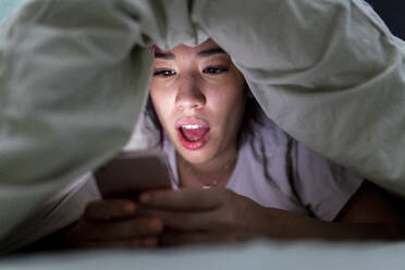 Surprised young woman using smart phone on bed at home - WPEF06842