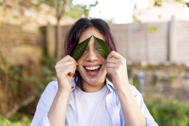 Glückliche Frau hält Blätter über die Augen im Garten - WPEF06850