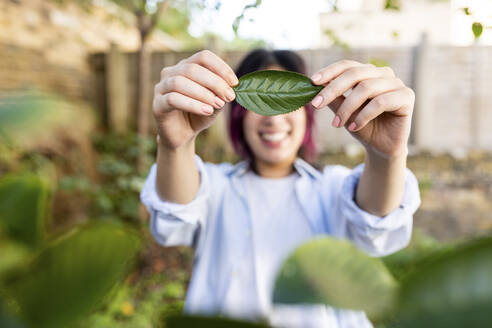 Glückliche Frau mit Blatt im Garten stehend - WPEF06852