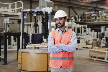 Smiling engineer wearing hardhat standing in industry - EBBF07377