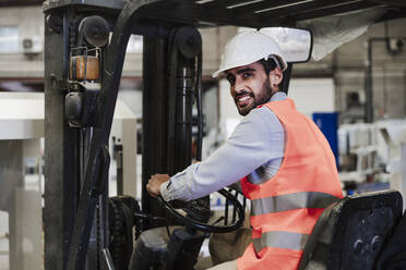 Glücklicher Ingenieur in Arbeitsschutzkleidung beim Gabelstaplerfahren in der Industrie - EBBF07378