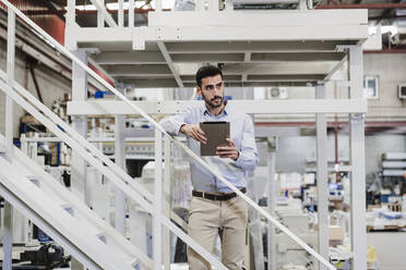 Contemplative businessman standing with tablet PC on staircase - EBBF07396