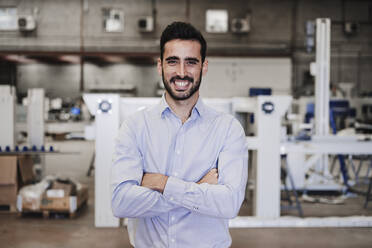 Happy engineer with arms crossed standing in industry - EBBF07404