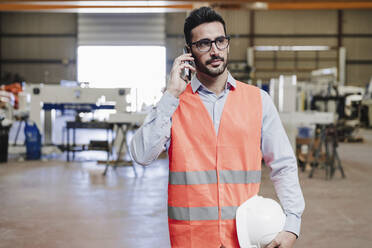 Engineer wearing protective workwear talking on smart phone in industry - EBBF07405