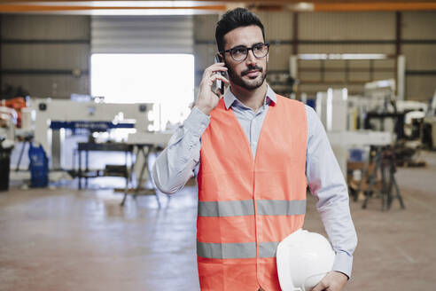 Ingenieur in Arbeitsschutzkleidung telefoniert mit seinem Smartphone in der Industrie - EBBF07405