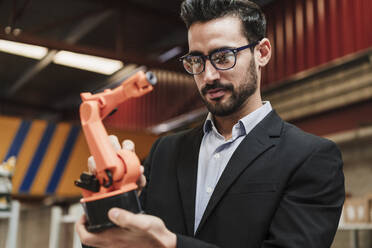 Businessman wearing eyeglasses examining robotic arm at industry - EBBF07434