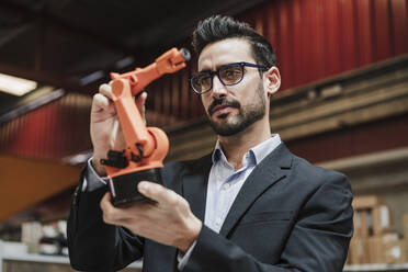 Businessman wearing eyeglasses examining robotic arm at factory - EBBF07435