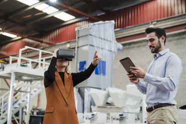 Businessman using tablet PC with colleague gesturing by wearing virtual reality simulator - EBBF07444