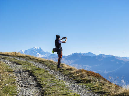 Ein älterer Mann fotografiert mit seinem Smartphone an einem sonnigen Tag im Vanoise-Nationalpark, Frankreich - LAF02786