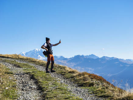 Senior man taking selfie through smart phone on sunny day at Vanoise national park, France - LAF02787