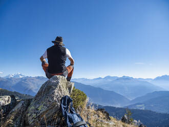 Senior man wearing hat sitting on rock in front of mountains at Vanoise national park, France - LAF02788