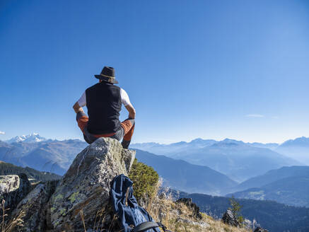 Älterer Mann mit Hut sitzt auf einem Felsen vor den Bergen im Vanoise-Nationalpark, Frankreich - LAF02788