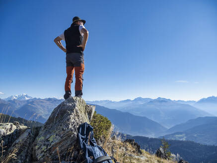 Älterer Mann mit Händen auf der Hüfte auf einem Felsen stehend unter blauem Himmel im Vanoise-Nationalpark, Frankreich - LAF02789