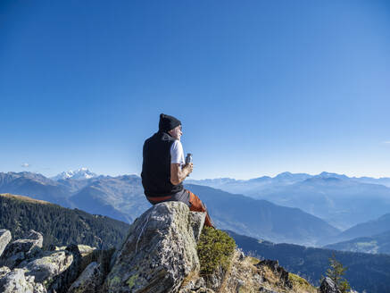 Älterer Mann mit Wasserflasche auf einem Felsen sitzend an einem sonnigen Tag im Vanoise-Nationalpark, Frankreich - LAF02791