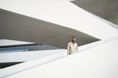 Contemplative man wearing headphones standing on staircase - RCPF01563