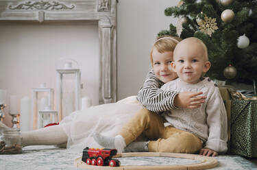 Geschwister sitzen gemeinsam am Weihnachtsbaum zu Hause - NDEF00247