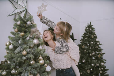 Daughter putting star on Christmas tree with mother at home - NDEF00256