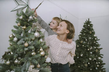 Smiling mother giving daughter piggyback ride to put star on Christmas tree - NDEF00257