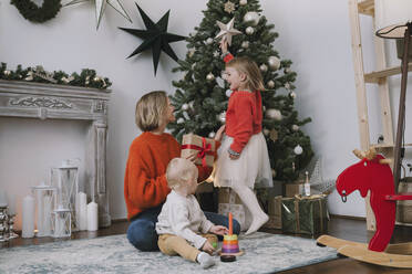 Tochter schmückt den Weihnachtsbaum mit sternförmigen Ornamenten zu Hause - NDEF00260