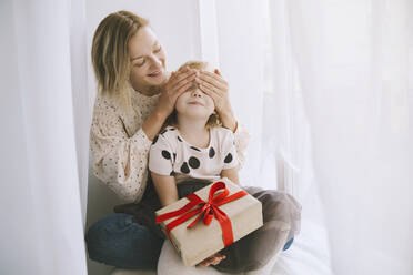 Mutter bedeckt die Augen ihrer Tochter mit einem Weihnachtsgeschenk vor einem Vorhang - NDEF00268