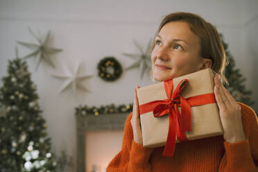 Besinnliche Frau mit Weihnachtsgeschenk zu Hause - NDEF00278