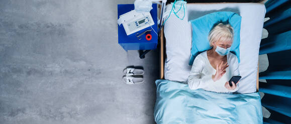 Draufsicht auf eine Covid-19-Patientin mit Maske und Smartphone im Krankenhausbett, Coronavirus-Konzept. - HPIF03093