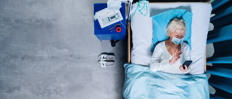 Top view of woman covid-19 patient with mask using smartphone in bed in hospital, coronavirus concept. - HPIF03093