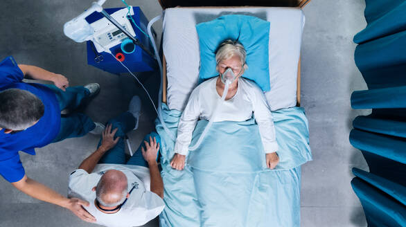 Top view of doctors and infected covid-19 patient with oxygen mask in bed in hospital, coronavirus concept. - HPIF03098