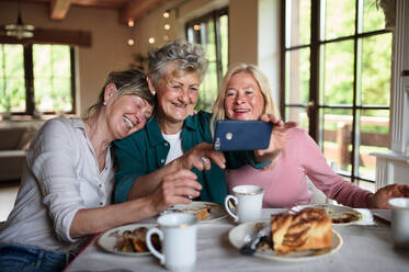 Glückliche ältere Freundinnen bei Kaffee und Kuchen und einem Selfie zu Hause. - HPIF03101