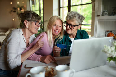 Happy senior friends using a laptop and credit card indoors at home, coffee time. - HPIF03105