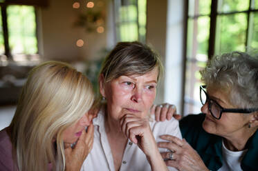 Female senior friends consloing a sad friend indoors at home. - HPIF03108