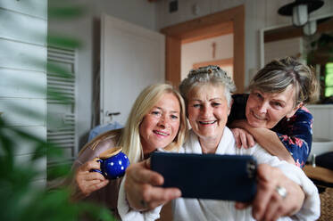 Glückliche ältere Frauen in Bademänteln, die ein Selfie zu Hause machen, Selfcare-Konzept. - HPIF03114