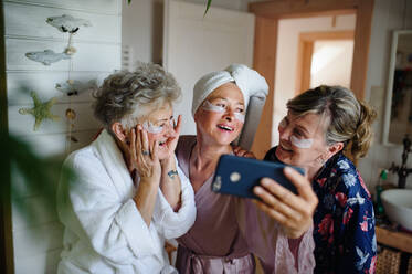 Glückliche ältere Frauen in Bademänteln, die ein Selfie zu Hause machen, Selfcare-Konzept. - HPIF03117