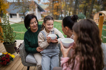 Zwei glückliche Schwestern mit einer Mutter und einer Großmutter, die im Herbst im Innenhof sitzen und Tee trinken. - HPIF03164