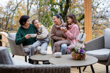 Zwei glückliche Schwestern mit einer Mutter und einer Großmutter, die im Herbst im Innenhof sitzen und Tee trinken. - HPIF03165