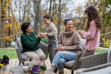 Zwei glückliche Schwestern mit einer Mutter und einer Großmutter, die im Herbst im Innenhof sitzen und Tee trinken. - HPIF03166