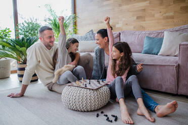 Two happy sisters with a mother and father sitting on floor and playing chess together at home - HPIF03199
