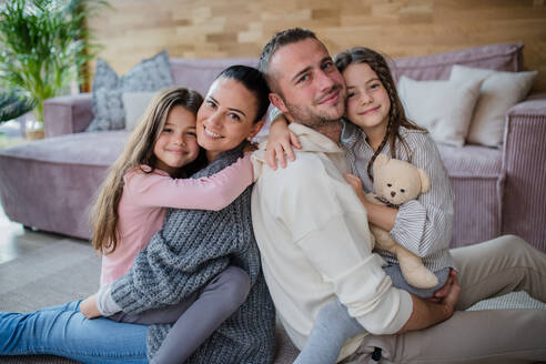 Zwei glückliche Schwestern mit einer Mutter und einem Vater, die auf dem Boden sitzen und sich umarmen und in die Kamera schauen - HPIF03202