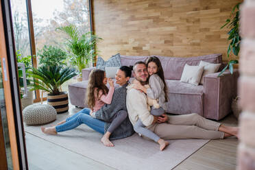 Two happy sisters with a mother and father sitting on floor hugging and looking at camera at home - HPIF03203