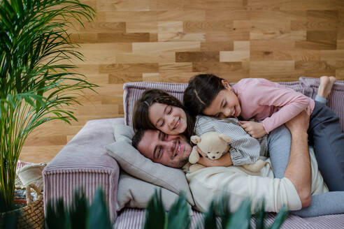 Zwei glückliche Schwestern, die sich mit ihrem Vater auf dem Sofa zu Hause amüsieren. - HPIF03205