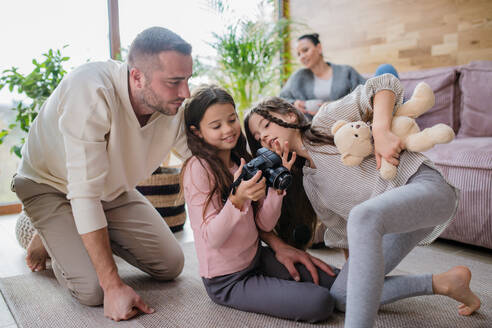 Zwei glückliche Schwestern mit ihrem Vater, die auf dem Boden sitzen und zu Hause lernen, mit der Kamera umzugehen - HPIF03210