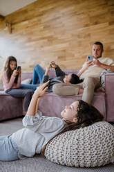 Eine Familie mit zwei kleinen Töchtern, alle benutzen ein Handy im Wohnzimmer. - HPIF03218