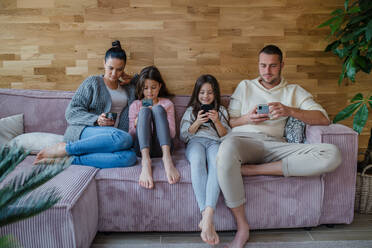 Eine Familie mit zwei kleinen Töchtern, alle benutzen ein Handy im Wohnzimmer. - HPIF03219