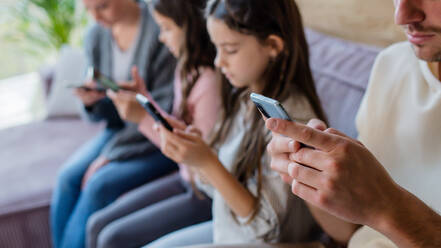 Eine Familie mit zwei kleinen Töchtern, alle benutzen ein Handy im Wohnzimmer. - HPIF03220