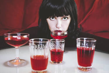 Frau trinkt rote alkoholische Getränke in verschiedenen Gläsern auf einem Tisch - SVCF00217