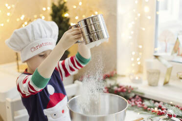 Junge mit Kochmütze siebt Mehl für Lebkuchen am Küchentisch - ONAF00291