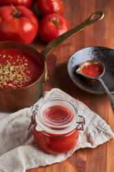 Pan and container with delicious homemade tomato sauce sprinkled with oregano placed on woven mat on wooden table in kitchen - ADSF41523